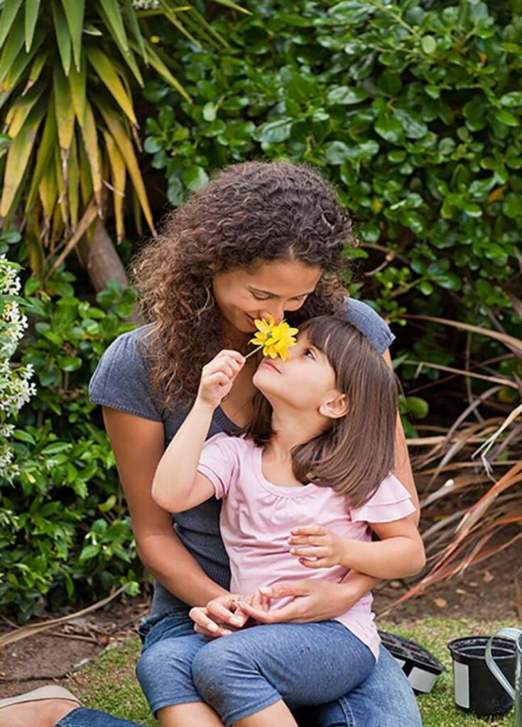 Madre e hija compartiendo una flor amarilla en un jardín